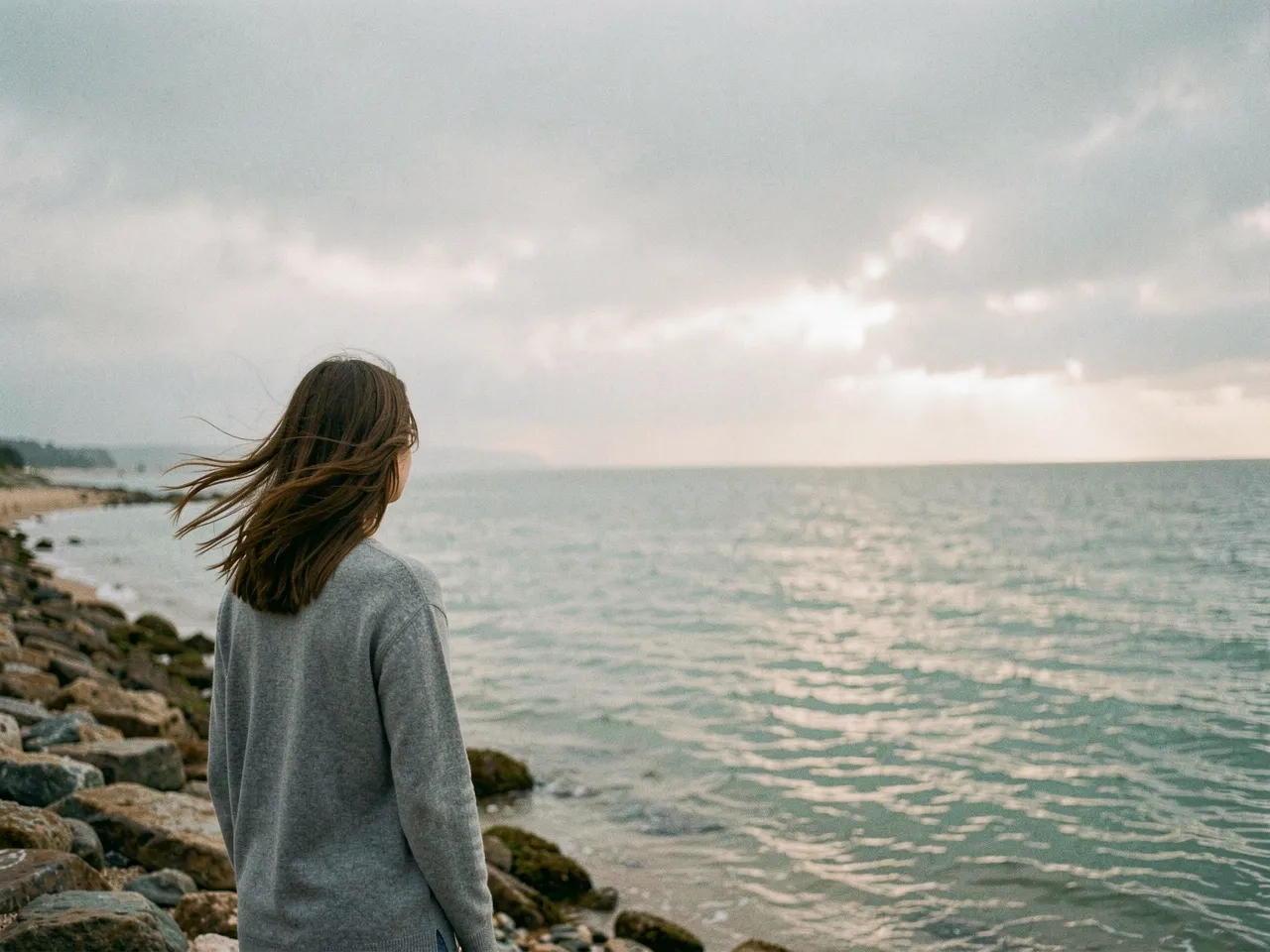 Woman standing on a rocky shoreline facing the sea
